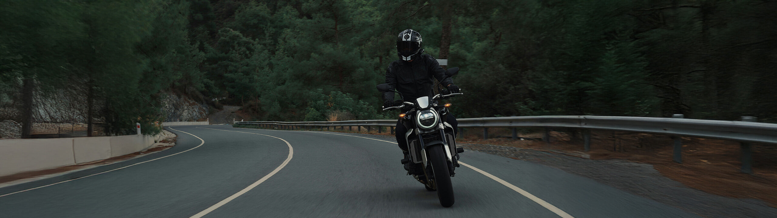 Motorradfahrer fährt auf einer dunklen Waldstraße.