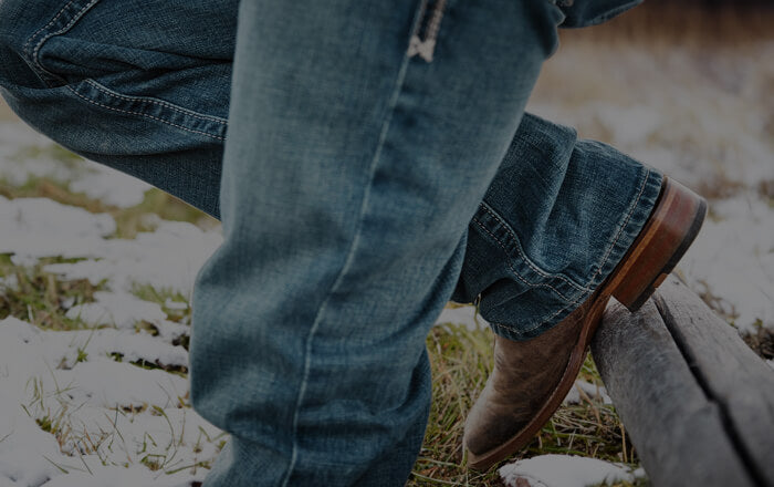 Herr mit Jeans und Stiefeln auf leicht schneebedeckter Wiese